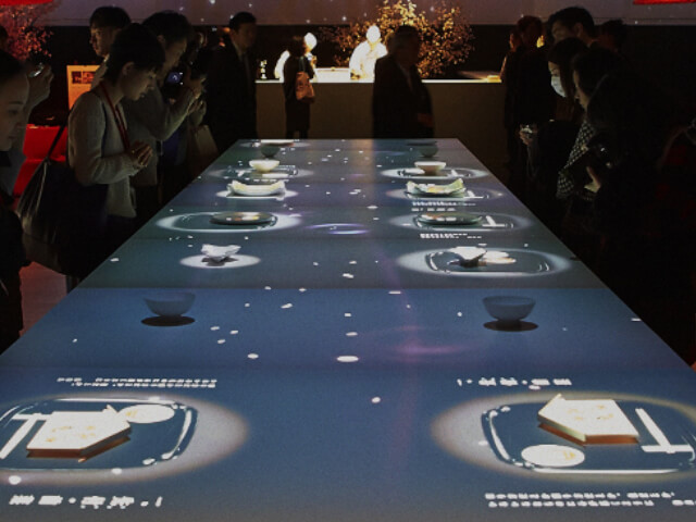 「食べるアート展 L’art de Rosanjin」のイベント会場に設置された 「季節の食卓プロジェクション」。テーブル上に置かれたさまざまな空の食器に、季節の料理が出現して彩られていきます。